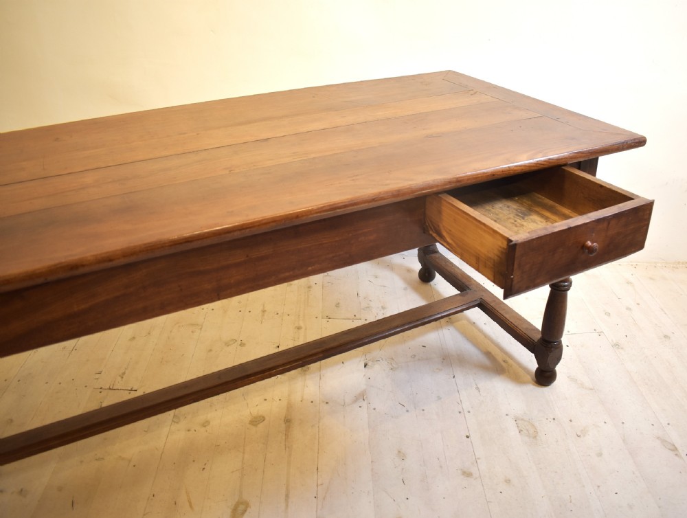 A rustic wooden farmhouse dining table featuring a plank top, a single side drawer, turned legs, and an H-stretcher base. View III