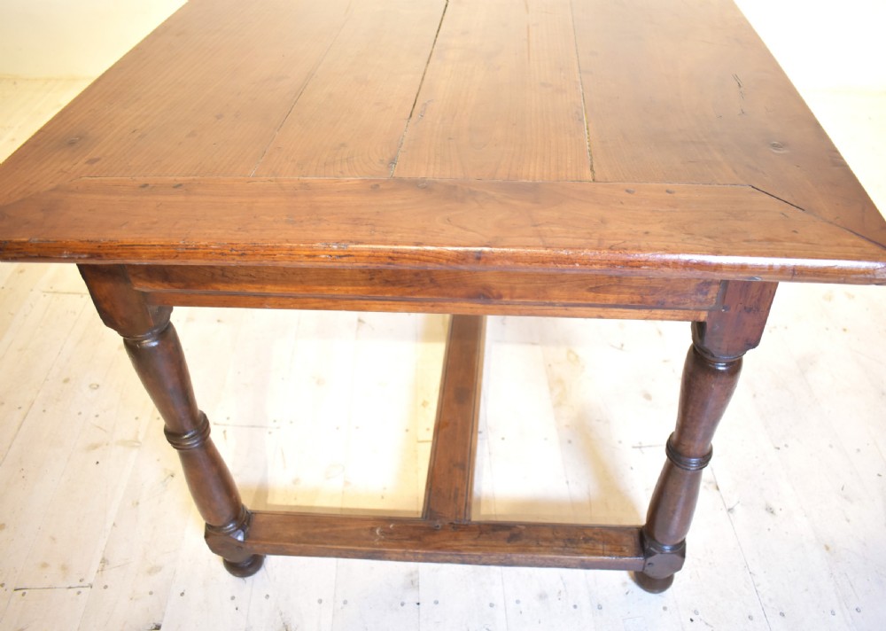 A rustic wooden farmhouse dining table featuring a plank top, a single side drawer, turned legs, and an H-stretcher base. View V