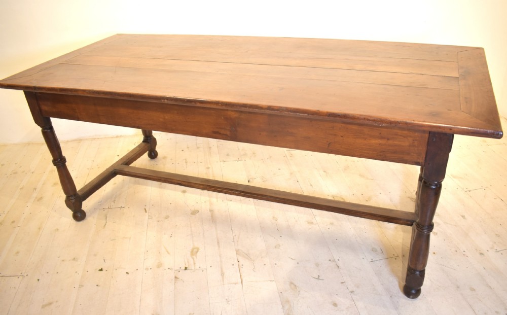 A rustic wooden farmhouse dining table featuring a plank top, a single side drawer, turned legs, and an H-stretcher base. View VI