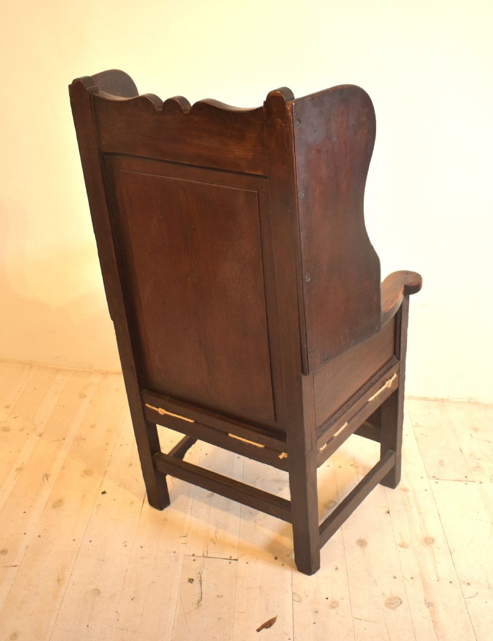 An antique dark oak lambing armchair with high winged sides, a panelled back, a storage base, and a patterned red seat cushion. View V