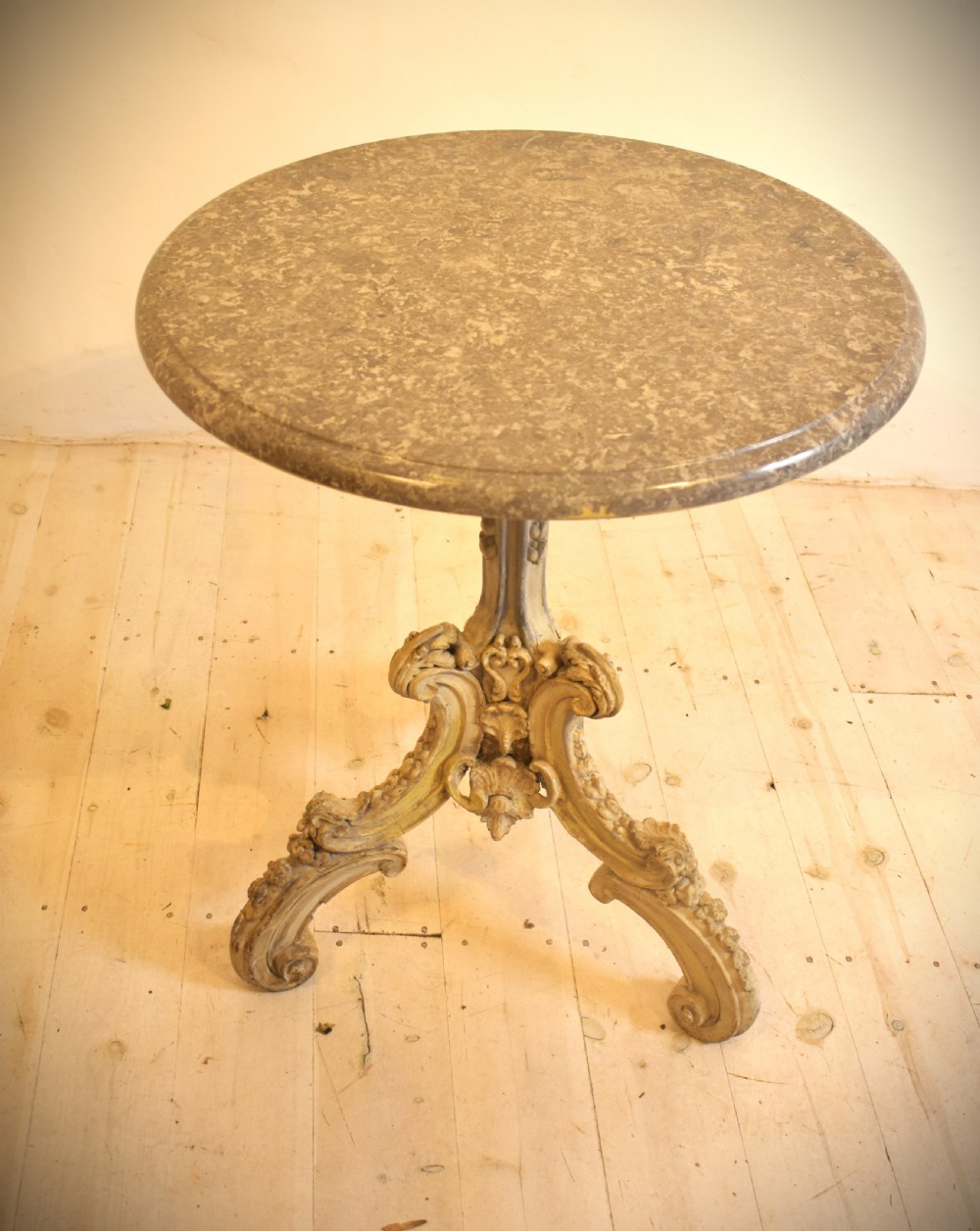 A circular grey marble top table supported by a carved cream painted pedestal base with tripod scroll feet. View II