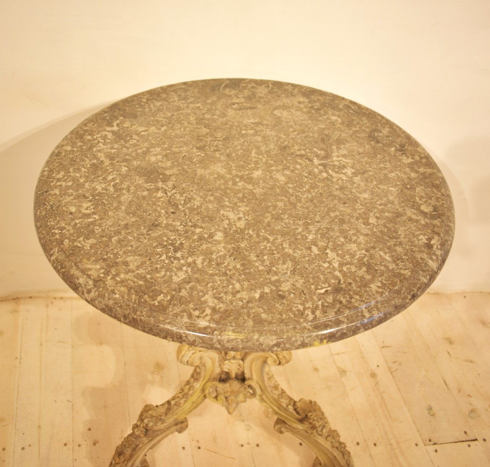 A circular grey marble top table supported by a carved cream painted pedestal base with tripod scroll feet. View V