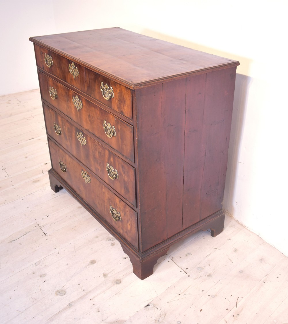A Georgian yew wood chest of drawers featuring four graduated long drawers with ornate brass drop handles and bracket feet. View IV