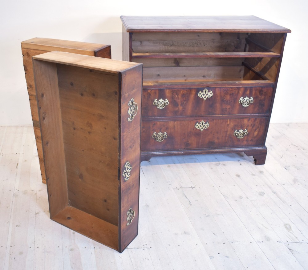 A Georgian yew wood chest of drawers featuring four graduated long drawers with ornate brass drop handles and bracket feet. View V