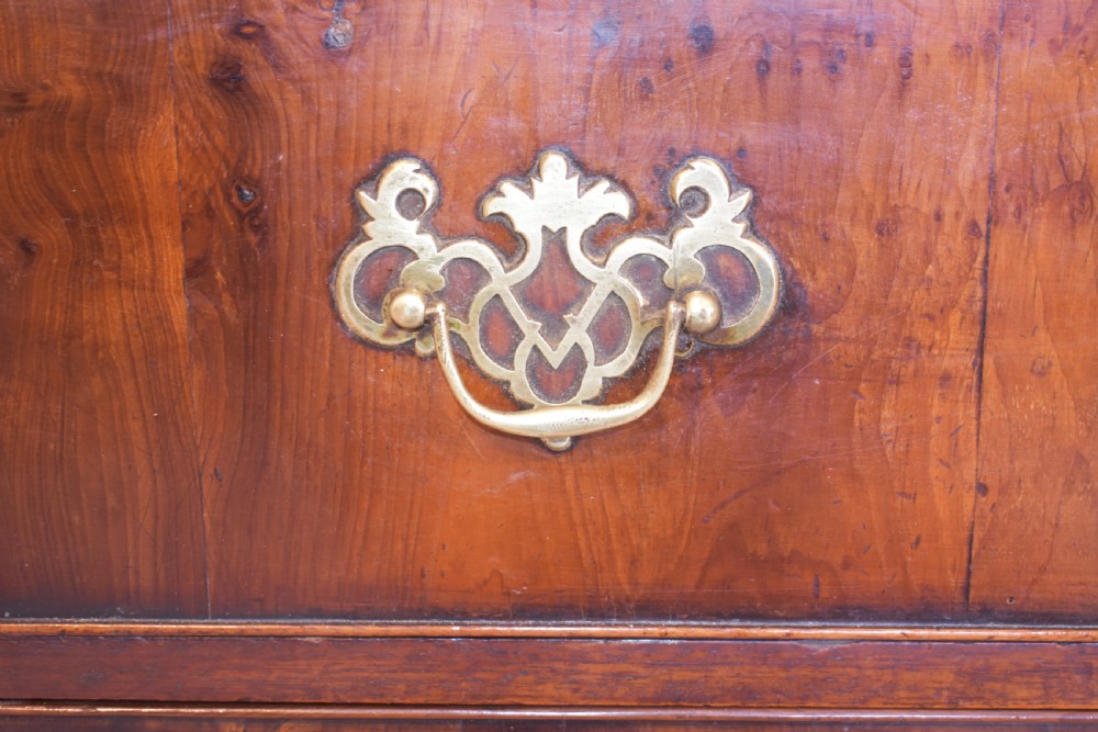 A Georgian yew wood chest of drawers featuring four graduated long drawers with ornate brass drop handles and bracket feet. View IX