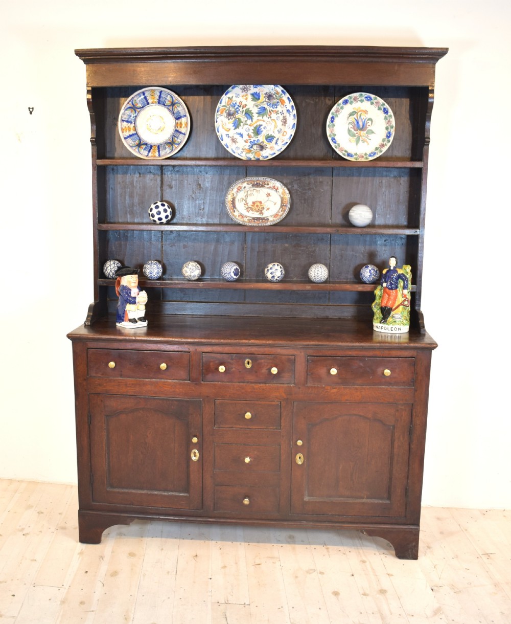 An antique dark oak Welsh dresser featuring a three-tier open plate rack above a base with multiple drawers, panelled cupboard doors, and brass knob handles. View II