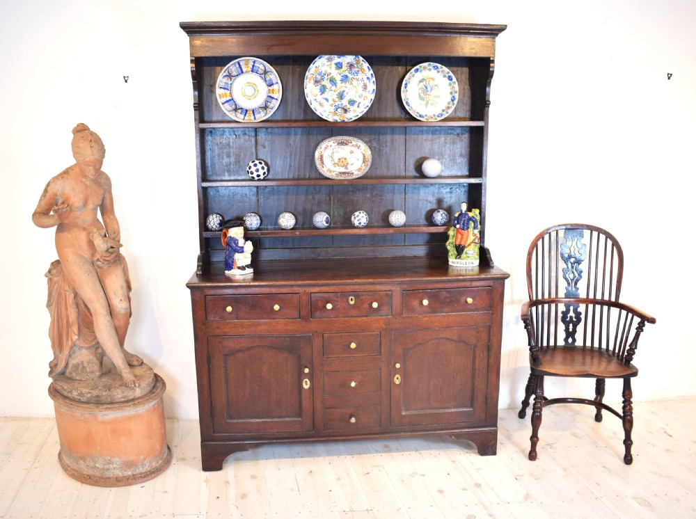 An antique dark oak Welsh dresser featuring a three-tier open plate rack above a base with multiple drawers, panelled cupboard doors, and brass knob handles. View IV