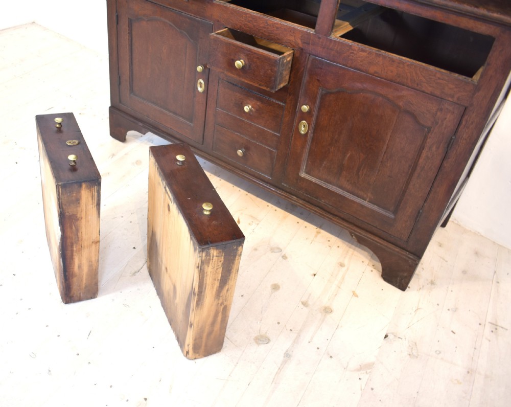 An antique dark oak Welsh dresser featuring a three-tier open plate rack above a base with multiple drawers, panelled cupboard doors, and brass knob handles. View V