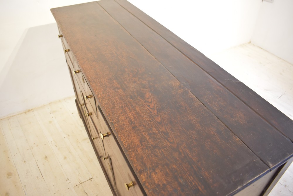 An antique dark oak Welsh dresser featuring a three-tier open plate rack above a base with multiple drawers, panelled cupboard doors, and brass knob handles. View VIII