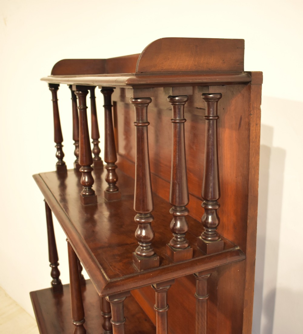 A dark mahogany waterfall bookcase featuring four graduated open shelves supported by turned spindles, curved side supports, and a base drawer with two brass knobs. View VII