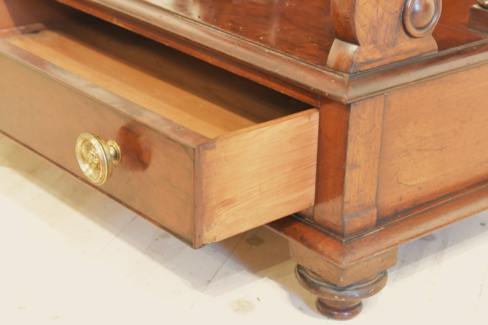 A dark mahogany waterfall bookcase featuring four graduated open shelves supported by turned spindles, curved side supports, and a base drawer with two brass knobs. View X
