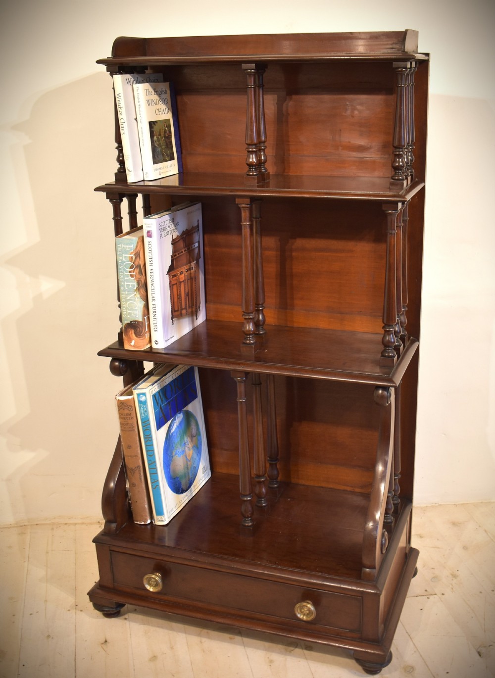 A dark mahogany waterfall bookcase featuring four graduated open shelves supported by turned spindles, curved side supports, and a base drawer with two brass knobs. View XII