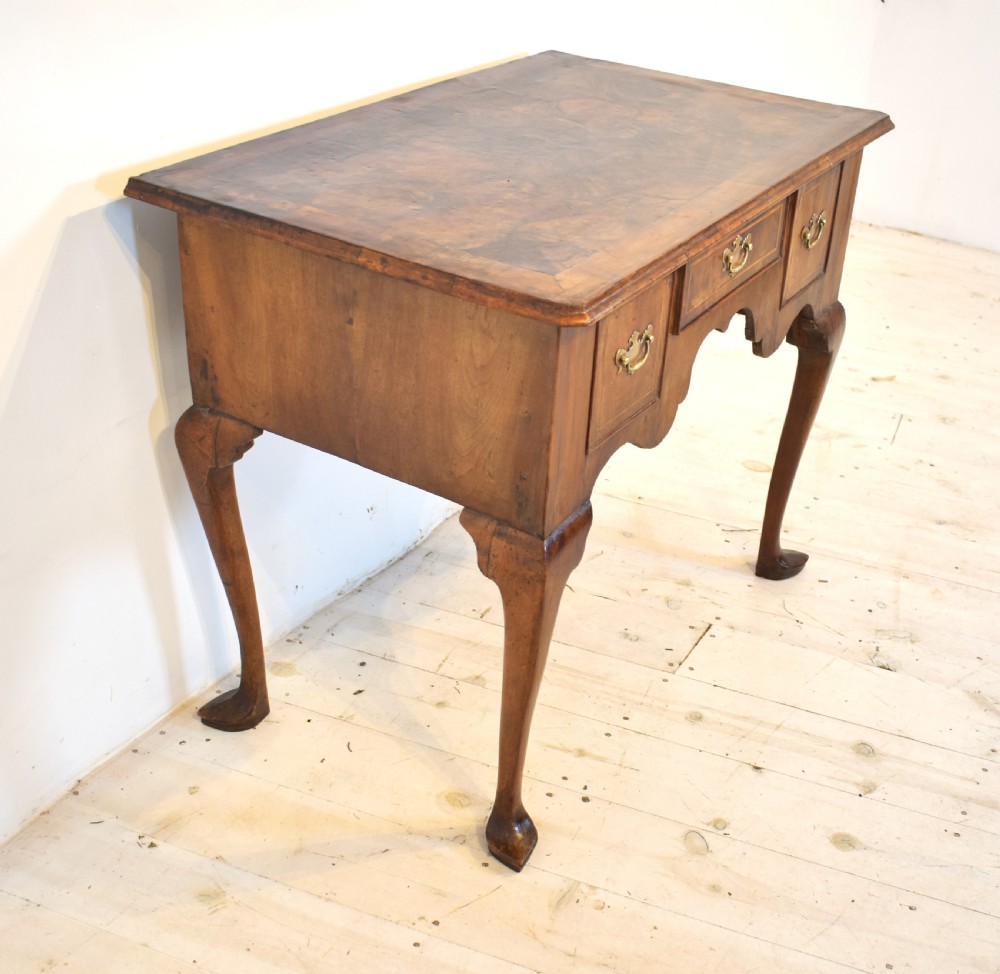 An antique Queen Anne style walnut lowboy featuring three crossbanded drawers with brass drop handles, a scalloped apron, and slender cabriole legs. View IV
