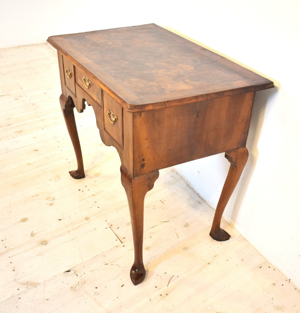 An antique Queen Anne style walnut lowboy featuring three crossbanded drawers with brass drop handles, a scalloped apron, and slender cabriole legs. View V