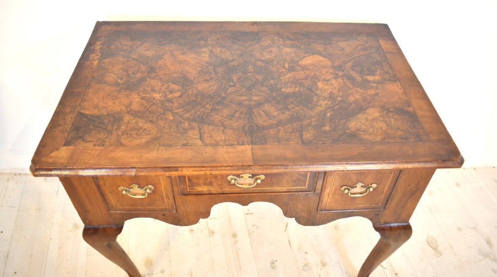 An antique Queen Anne style walnut lowboy featuring three crossbanded drawers with brass drop handles, a scalloped apron, and slender cabriole legs. View VI