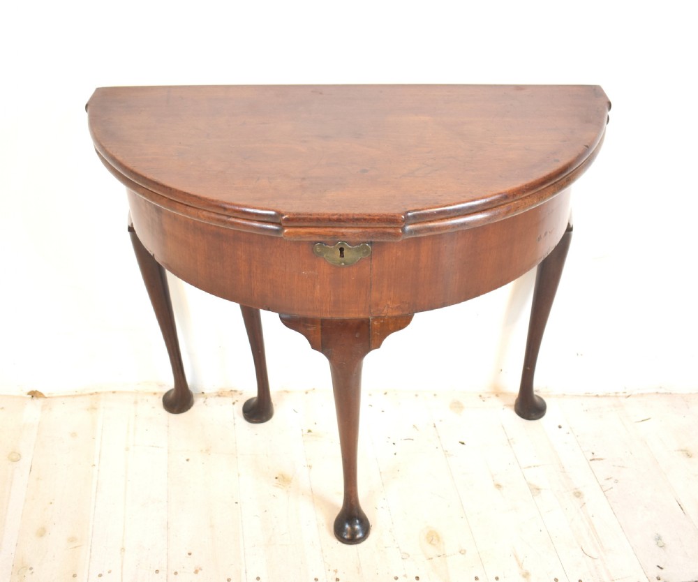An early 18th-century mahogany demi-lune fold-over tea table featuring slender cabriole legs with pad feet and a central brass keyhole escutcheon.