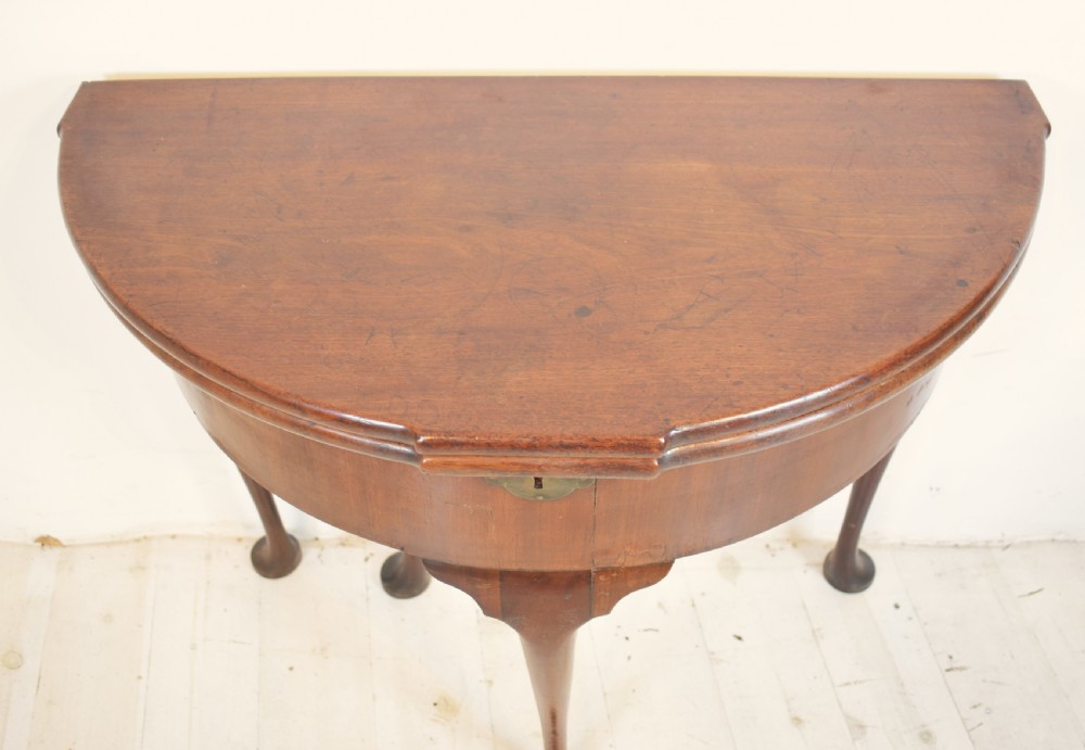 An early 18th-century mahogany demi-lune fold-over tea table featuring slender cabriole legs with pad feet and a central brass keyhole escutcheon. View II