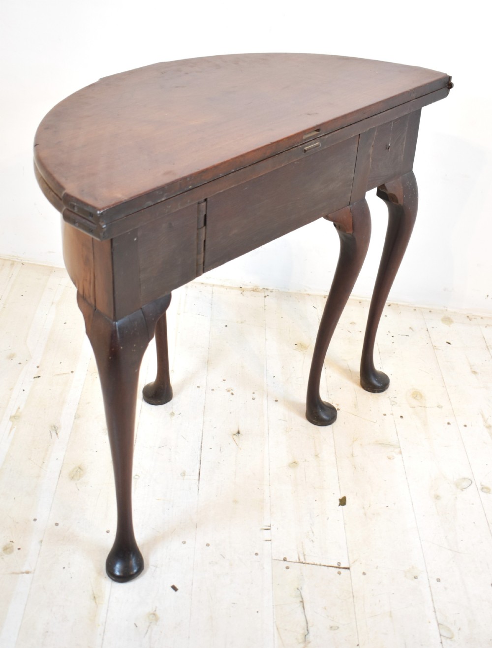 An early 18th-century mahogany demi-lune fold-over tea table featuring slender cabriole legs with pad feet and a central brass keyhole escutcheon. View IV