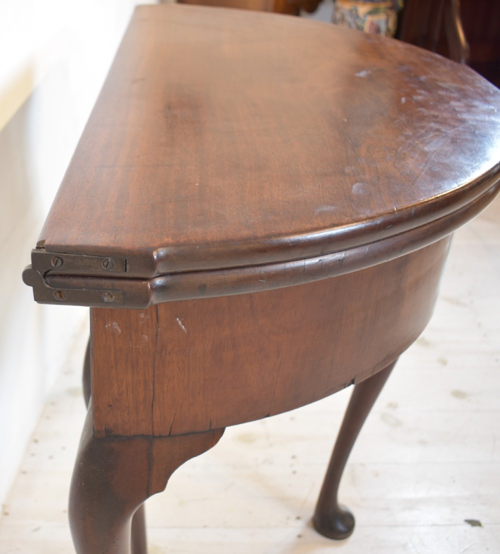 An early 18th-century mahogany demi-lune fold-over tea table featuring slender cabriole legs with pad feet and a central brass keyhole escutcheon. View VII