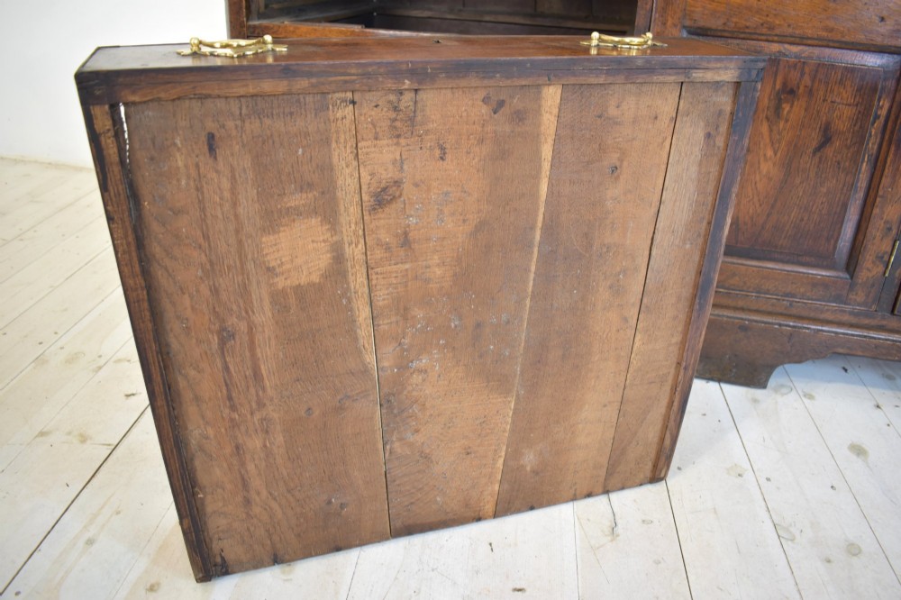 An eighteenth-century dark oak Lancashire dresser base featuring a central fielded panel cupboard door flanked by multiple drawers with brass batwing drop handles. View V