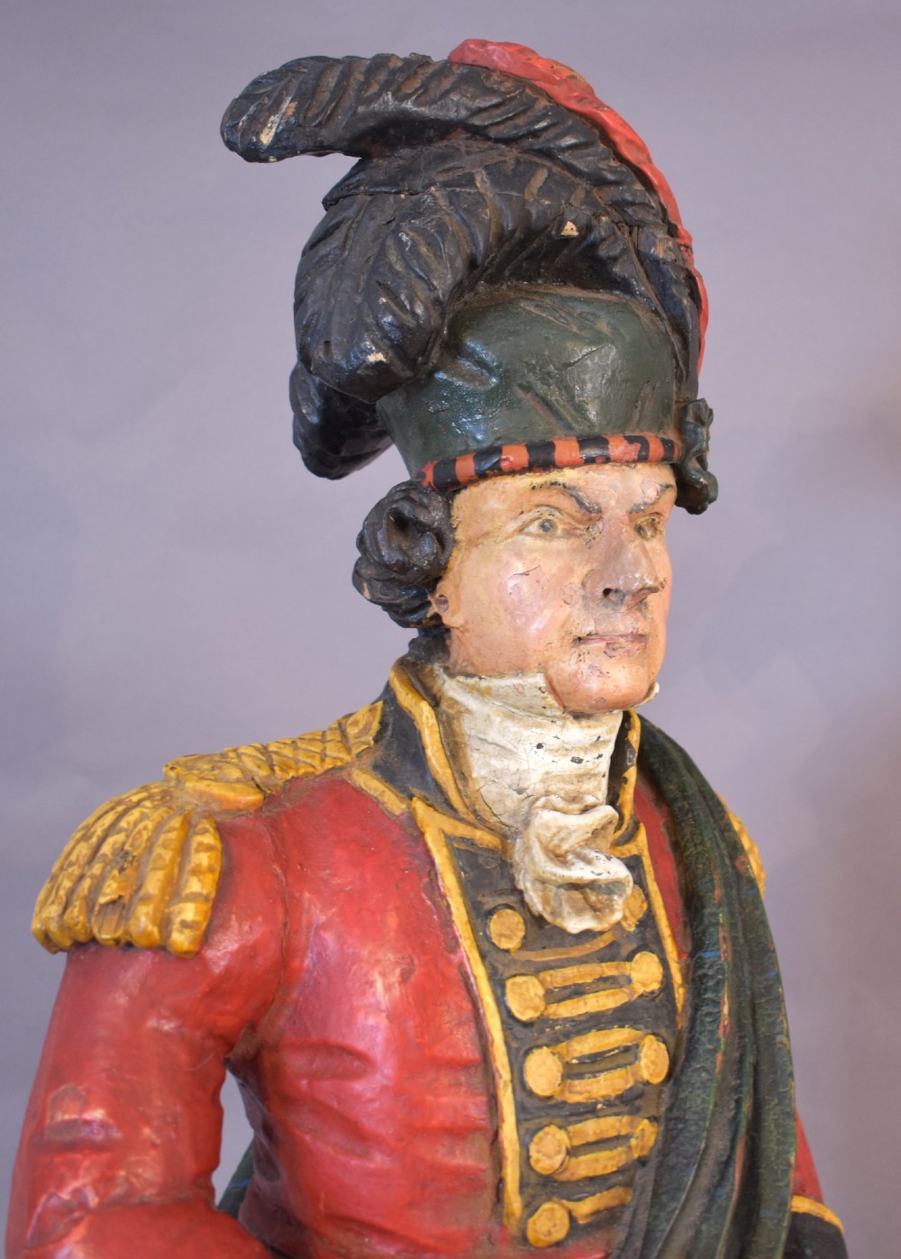 A carved and painted wooden figure of a Scottish Highlander soldier wearing a red jacket, kilt, and feathered bonnet. View V