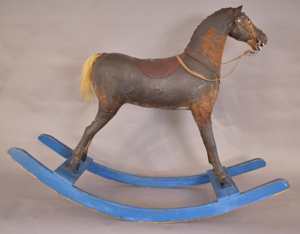 An antique wooden rocking horse with a dark distressed body, leather saddle, and yellowed hair tail, mounted on bright blue wooden bow rockers.