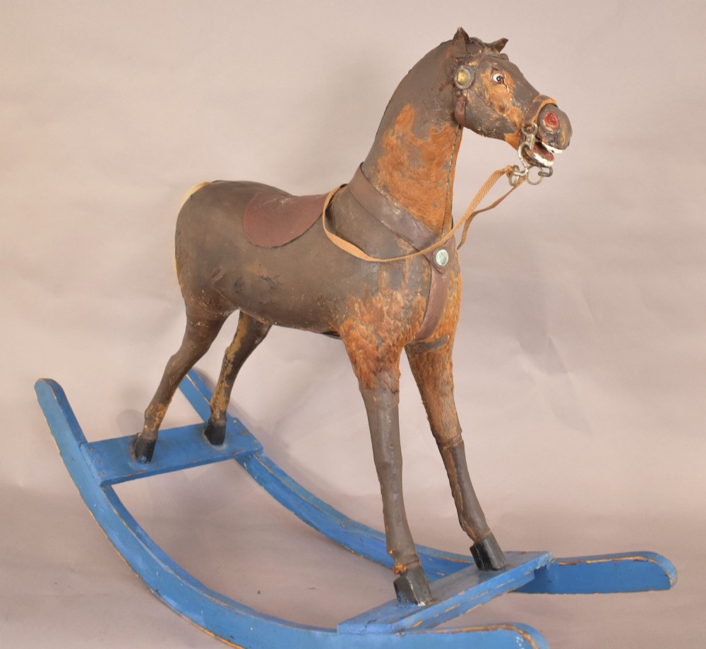 An antique wooden rocking horse with a dark distressed body, leather saddle, and yellowed hair tail, mounted on bright blue wooden bow rockers. View IV
