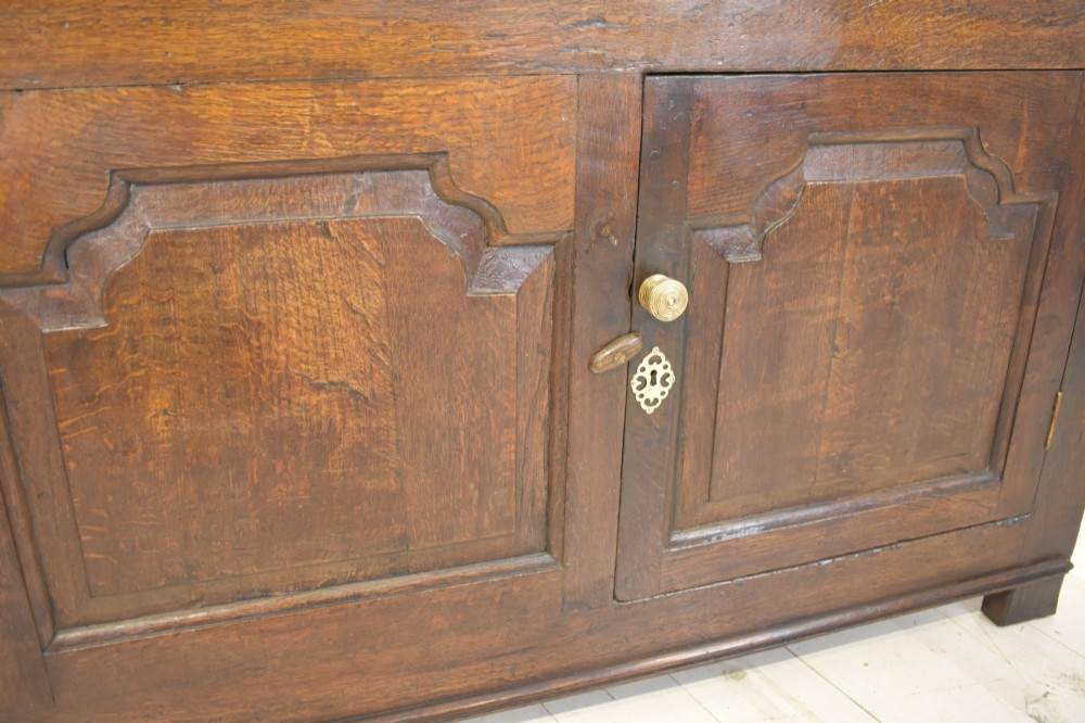 An 18th-century dark oak dresser base featuring three top drawers with brass handles above three cupboard doors with shaped fielded panels. View VII