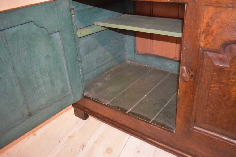 An 18th-century dark oak dresser base featuring three top drawers with brass handles above three cupboard doors with shaped fielded panels. View X