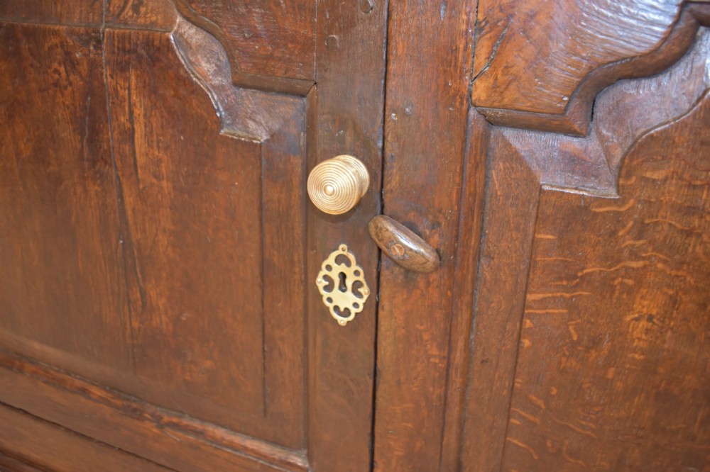 An 18th-century dark oak dresser base featuring three top drawers with brass handles above three cupboard doors with shaped fielded panels. View XI