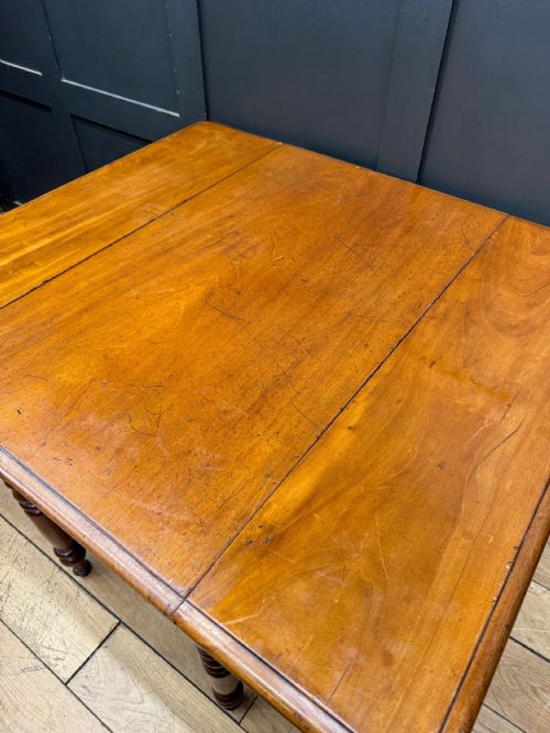 fig 1. An antique mahogany drop leaf table with two raised side flaps and four turned legs set against a dark panelled backdrop.