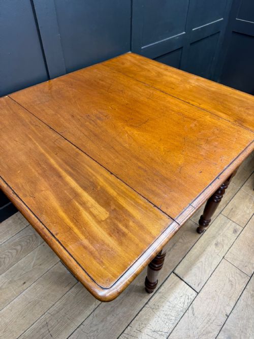 fig 2. An antique mahogany drop leaf table with two raised side flaps and four turned legs set against a dark panelled backdrop.