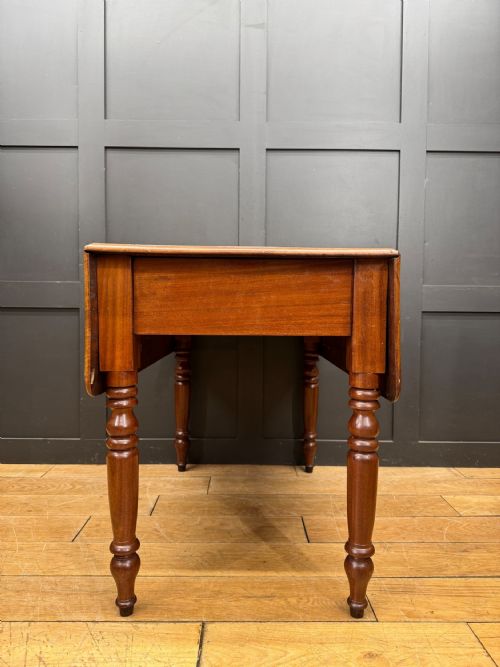 fig 3. An antique mahogany drop leaf table with two raised side flaps and four turned legs set against a dark panelled backdrop.