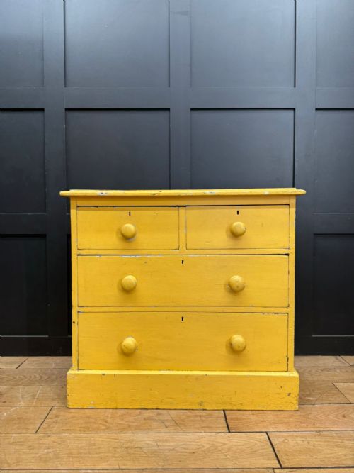 fig 1. An antique yellow painted pine chest of drawers featuring two short drawers over two long drawers with matching turned wooden knobs and a solid plinth base.