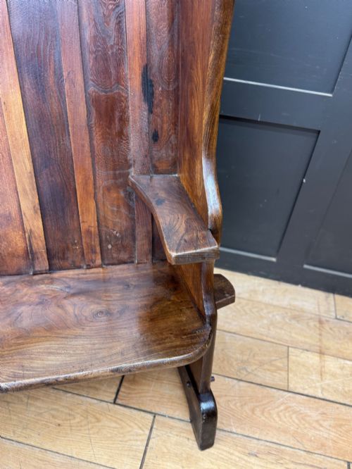 fig 3. A curved antique elm wooden settle pew featuring a slatted high back, shaped side wings, and visible pegged joinery.