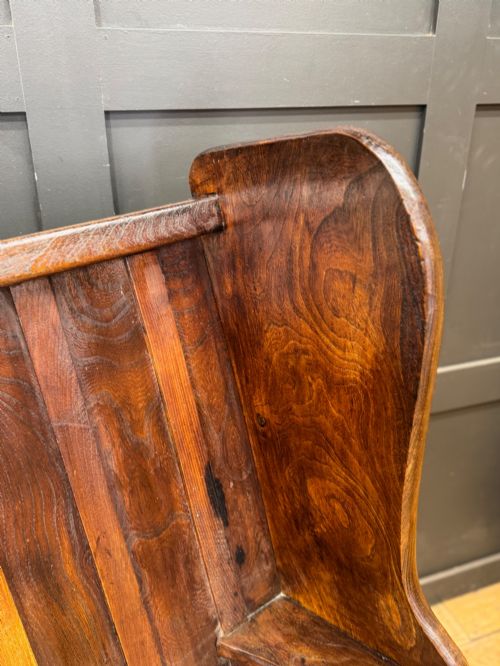 fig 4. A curved antique elm wooden settle pew featuring a slatted high back, shaped side wings, and visible pegged joinery.