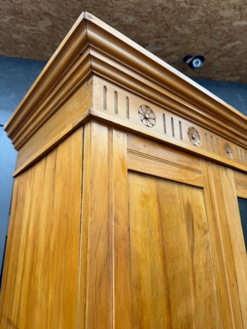 fig 1. A tall Edwardian satinwood wardrobe featuring a central mirrored door, panelled side doors, a carved rosette frieze, and a wide drawer at the base.