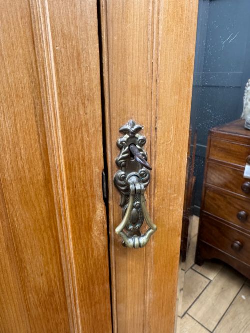 fig 2. A tall Edwardian satinwood wardrobe featuring a central mirrored door, panelled side doors, a carved rosette frieze, and a wide drawer at the base.
