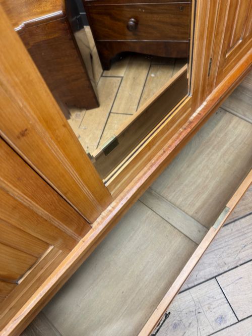 fig 5. A tall Edwardian satinwood wardrobe featuring a central mirrored door, panelled side doors, a carved rosette frieze, and a wide drawer at the base.