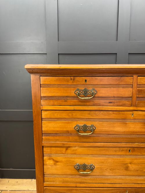 fig 1. A Victorian antique walnut chest featuring two short over three long drawers with ornate brass handles and reeded drawer fronts resting on a solid plinth base.