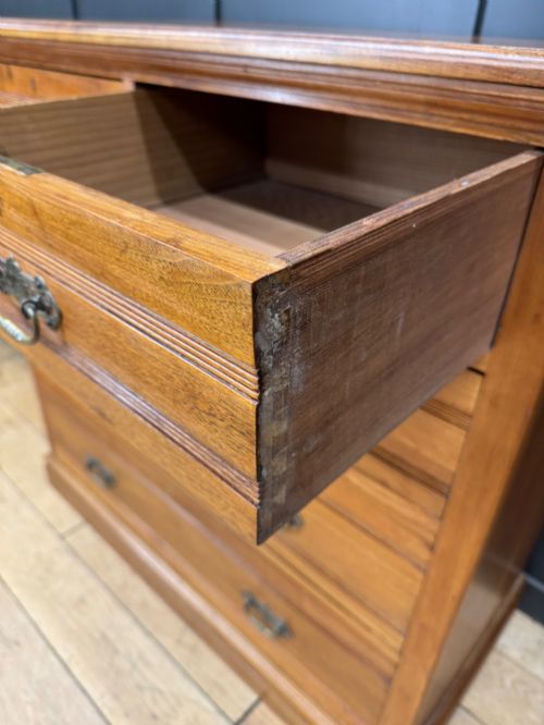 fig 2. A Victorian antique walnut chest featuring two short over three long drawers with ornate brass handles and reeded drawer fronts resting on a solid plinth base.