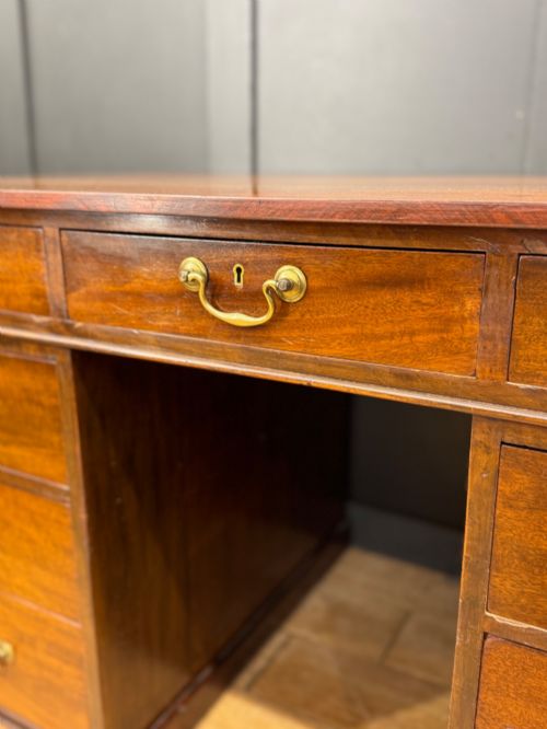 fig 4. An antique mahogany pedestal desk featuring three frieze drawers, twin drawer pedestals with brass drop handles, and a solid plinth base.