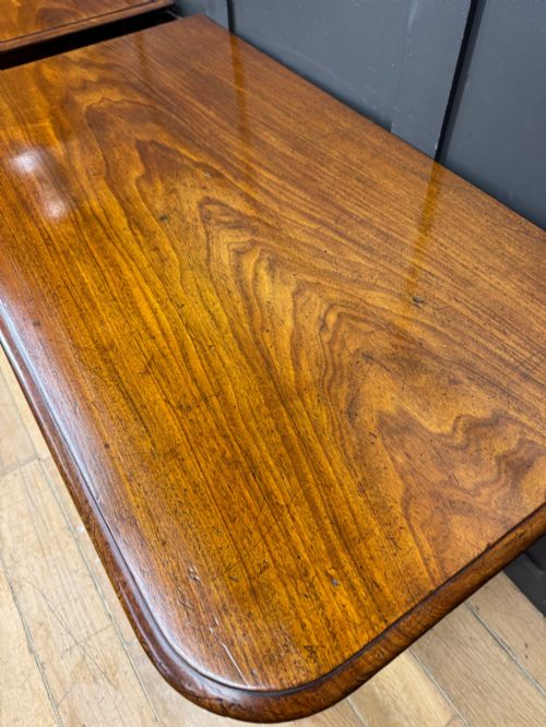 fig 1. A matching pair of dark mahogany side tables featuring turned legs and brass castors standing against a panelled wall.