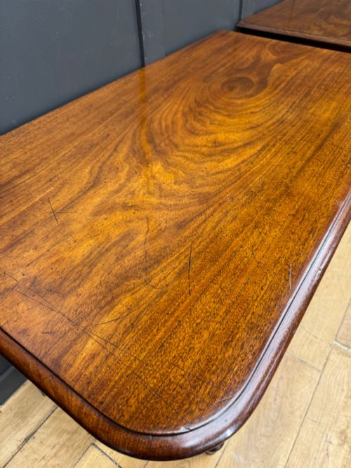fig 2. A matching pair of dark mahogany side tables featuring turned legs and brass castors standing against a panelled wall.