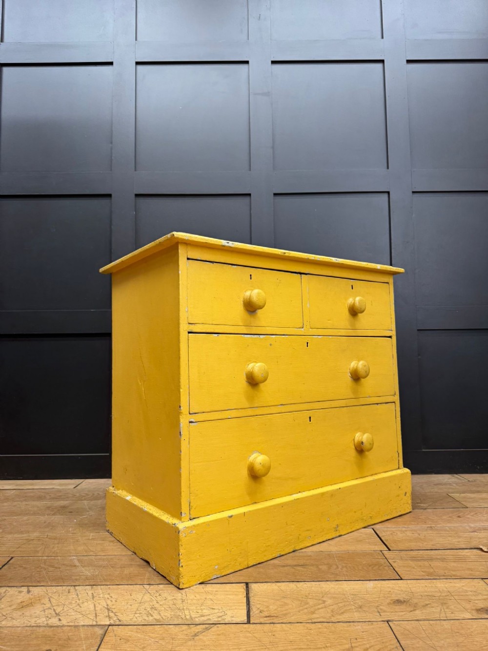 An antique yellow painted pine chest of drawers featuring two short drawers over two long drawers with matching turned wooden knobs and a solid plinth base.
