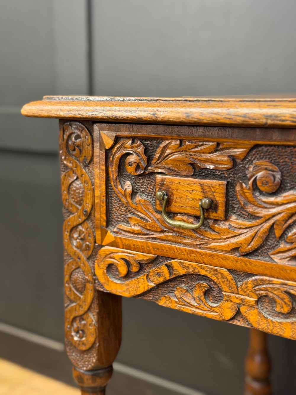 An antique carved oak side table featuring turned legs, a single carved drawer with brass handles, and lower stretchers. View VII
