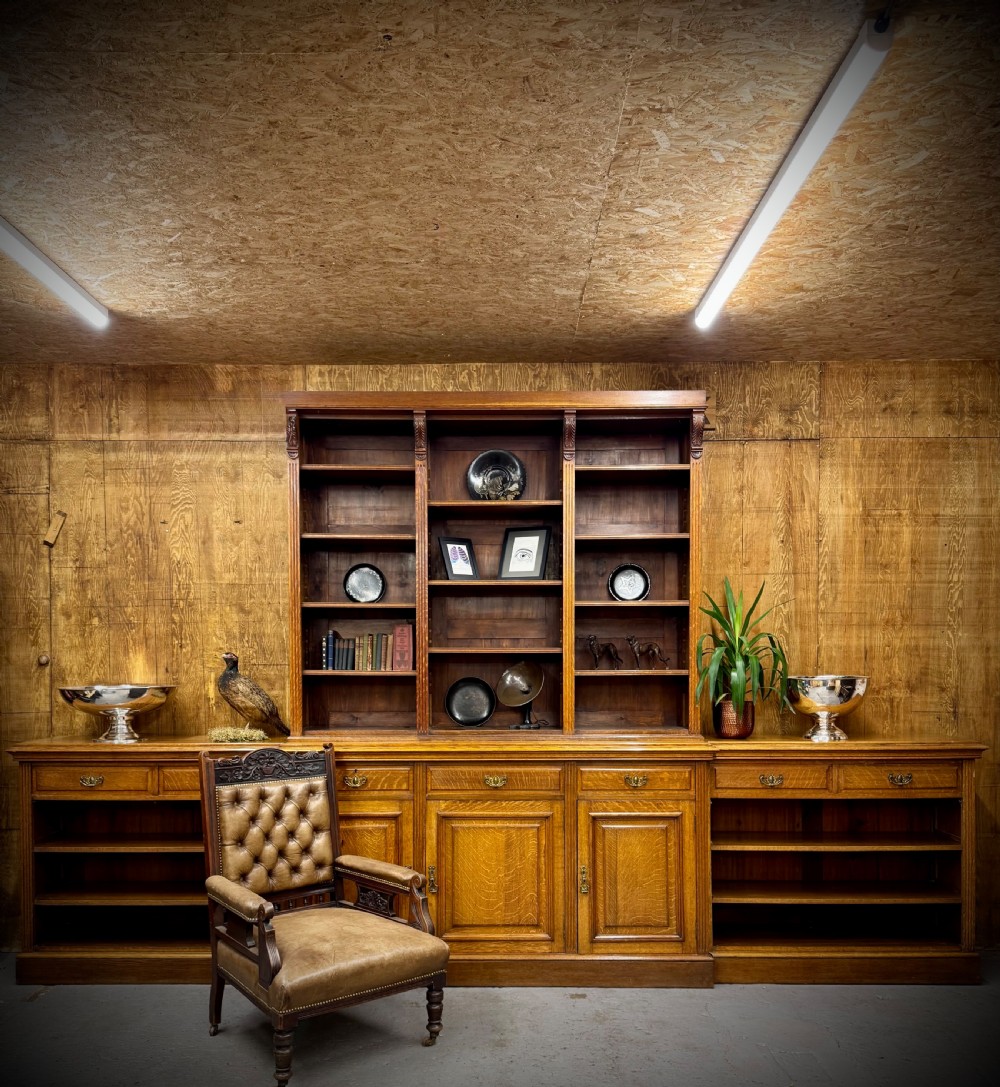 A large Victorian solid oak breakfront library bookcase with central panelled cupboard doors, drawers, open adjustable shelving, and carved corbels. View II