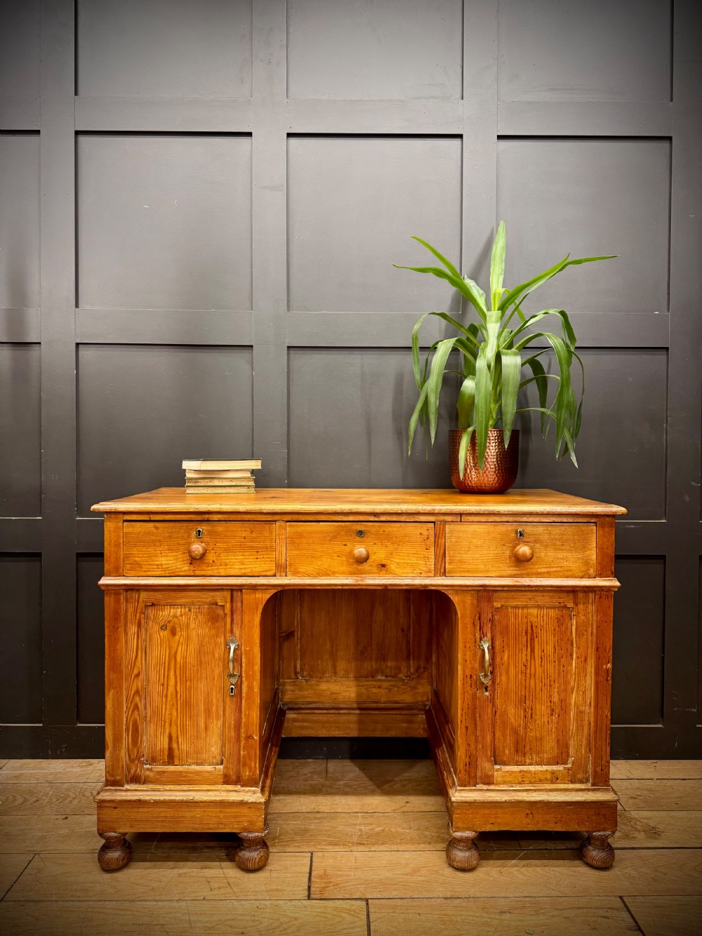 An antique pine pedestal desk featuring three top frieze drawers over two cupboard pedestals, resting on turned bun feet. View IV