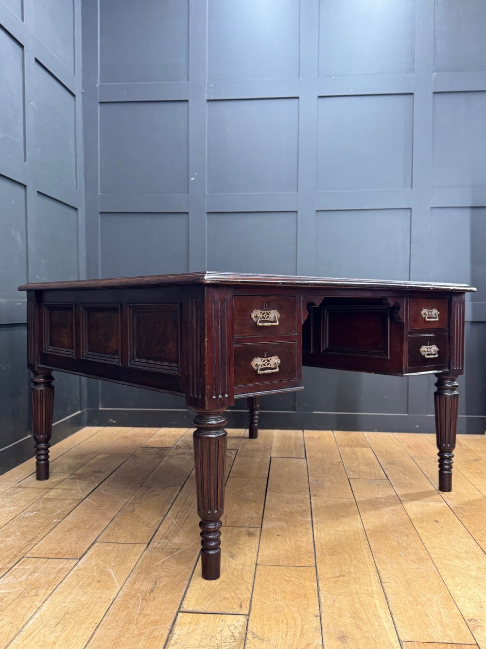 A dark mahogany partners desk with fluted turned legs, panelled sides, and multiple drawers fitted with brass handles.