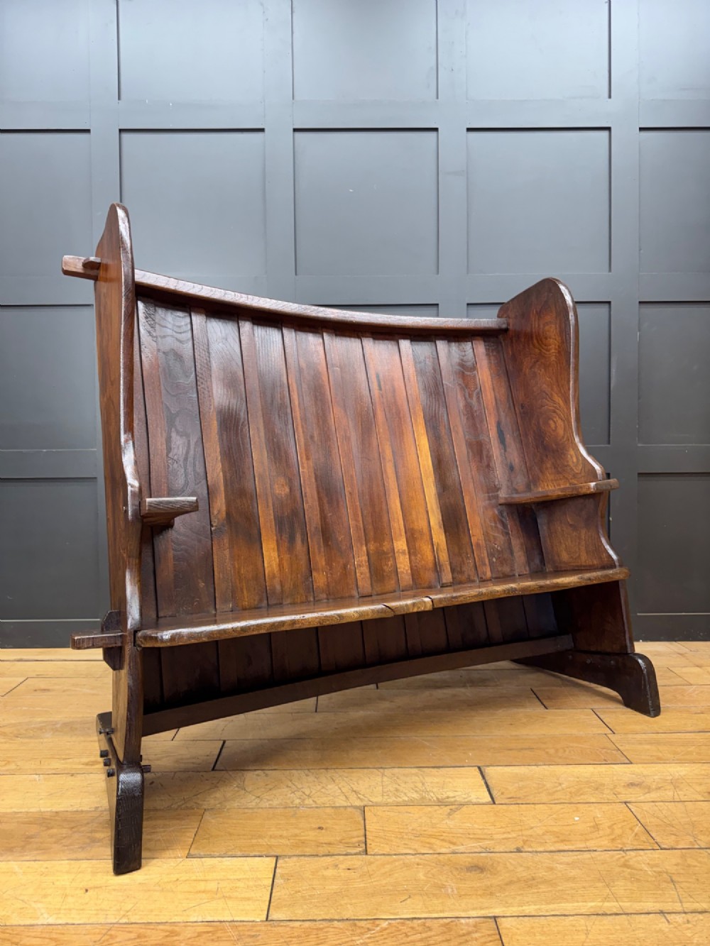 A curved antique elm wooden settle pew featuring a slatted high back, shaped side wings, and visible pegged joinery.